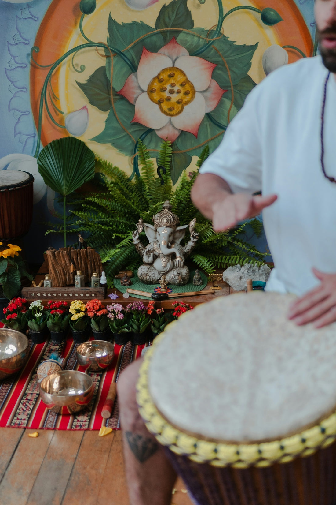 Man playing drum in front of ganesha statue.